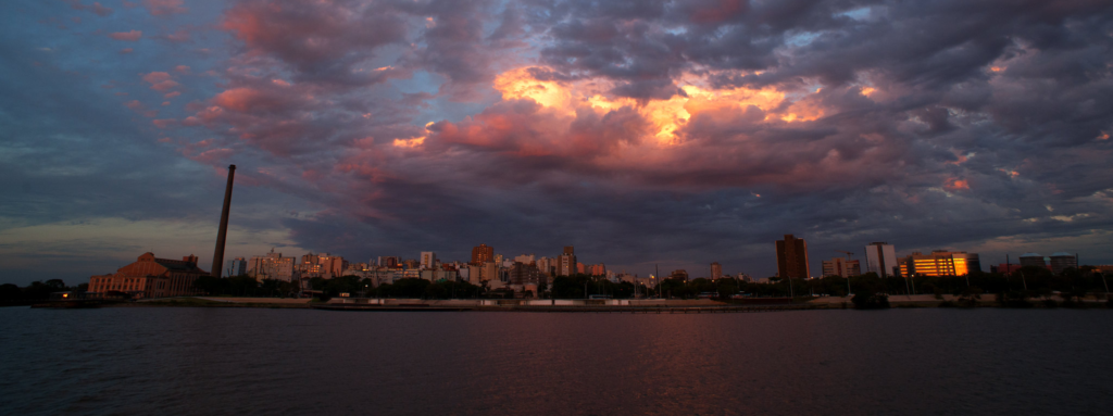 Paisagem panorâmica de Porto Alegre vista do rio, com a Usina do Gasômetro mais à esquerda, em um final de tarde parcialmente nublado