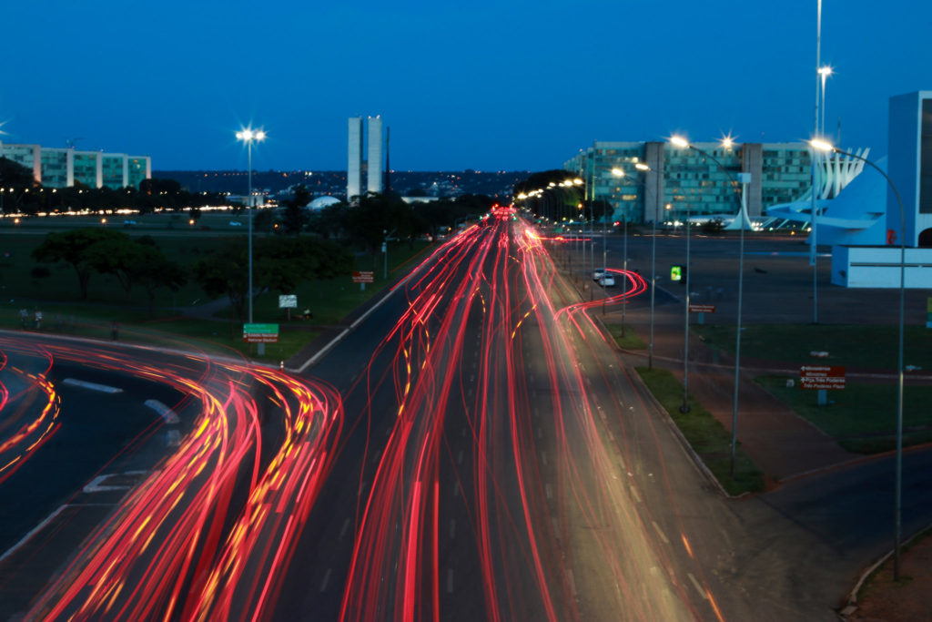 Imagem à noite de brasília, mostrando faróis vermelhos do trânsito com palácio ao fundo